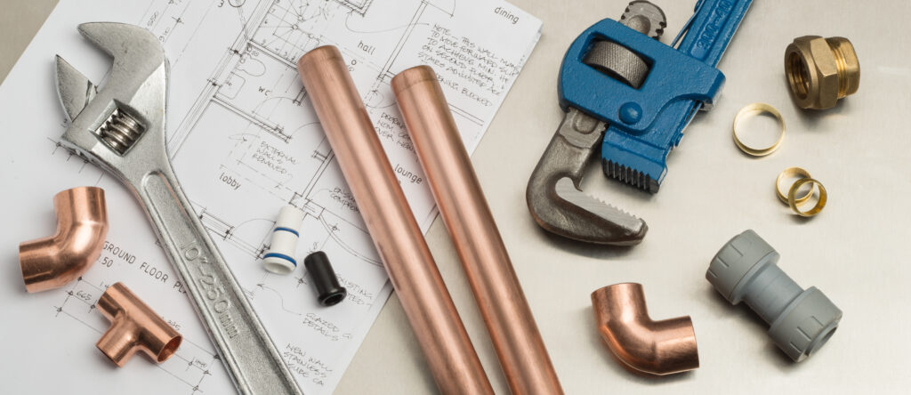 Pipes and plumbing tools lying on top of home plans