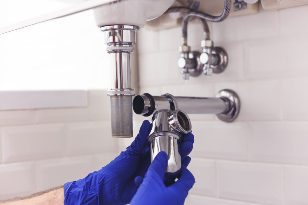 A plumber wrenching on a pipe underneath a sink