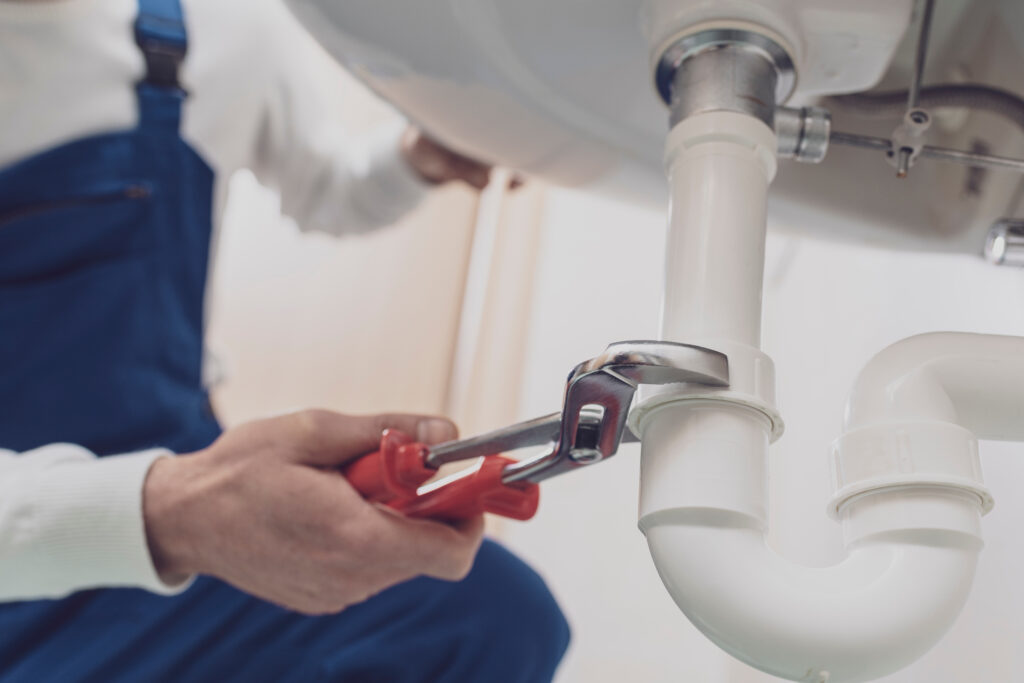 A plumber wrenching on a pipe underneath a sink